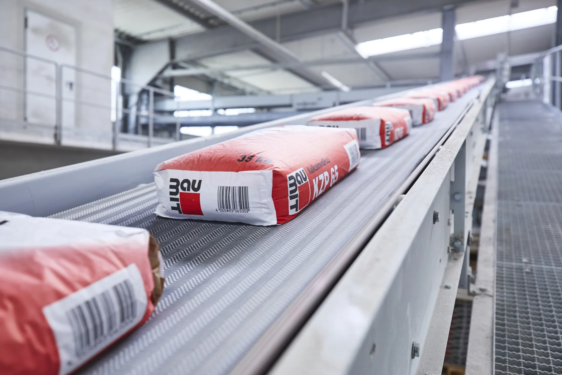 Zementsäcke der Marke Baumit auf Förderband in moderner Industriehalle bei der automatisierten Verarbeitung.