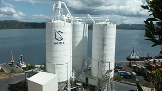 An einem Schüttgutterminal mit drei Stahlsilos werden Schiffe beladen.