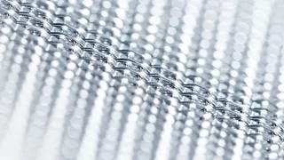 Macro shot of a shiny stainless steel wire mesh by Haver & Boecker with diagonal structure and reflective light points.
