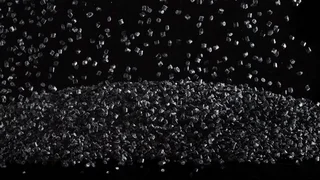 Black plastic granules fall in an arc and form a pile against a black background, a symbolic image for plastics engineering.