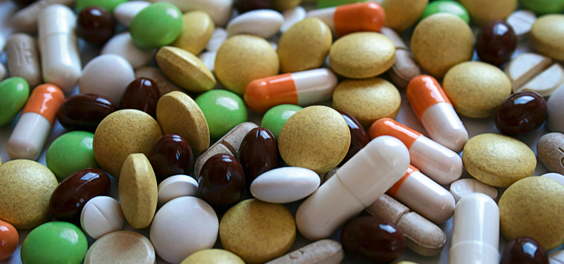 Various colorful tablets, capsules and dragees from the pharmaceutical industry lie close together on a white surface.