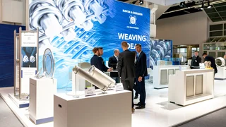 Moderne Haver & Boecker Messepräsentation mit Drahtgeweben, Filterelementen und Besuchern im Gespräch auf einem hellen, technologischen Messestand.