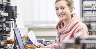 Eine duale Studentin sitzt am Laptop vor einem Schaltschrank.