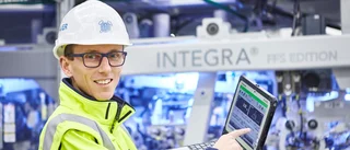 Ein Mitarbeiter mit Schutzhelm, Brille und gelber Sicherheitsjacke demonstriert Leistungsdaten auf einem Laptop.