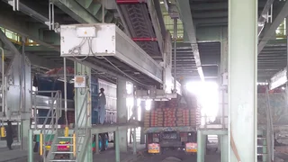 Ein Mann ist damit beschäftigt, mit Unterstützung eines halbautomatischen Beladesystems befüllte Säcke mit Baustoffen auf eine offene Ladefläche zu packen.