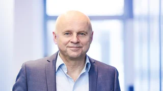Portrait of a smiling Mr. John in a suit in front of a blurred, modern office background at Haver & Boecker.