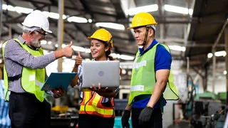 Drei Personen in Schutzbekleidung stehen an Laptop und strecken lächelnd die Daumen hoch.