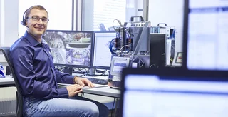 Technisch versiert: Ein Mann im blauen Hemd sitzt mit Headset vor mehreren Bildschirmen.
