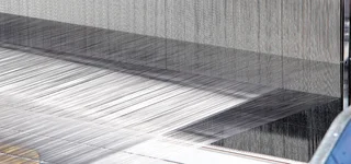 Fine metal wires are arranged on a loom to produce technical wire mesh at Haver & Boecker; detailed view of the warping process.