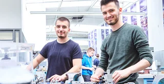 Zwei Auszubildende stehen in der Lehrwerkstatt an ihrer Werkbank.