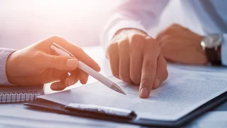 Zwei Personen zeigen auf ein Dokument und besprechen dieses.