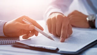 Zwei Personen zeigen auf ein Dokument und besprechen dieses.